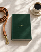 The Olfie Book in forest green, flat on linen beside a lead and a coffee